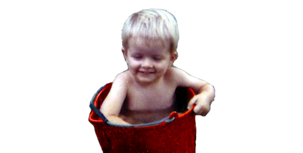 A 3 year old Tim Bloom sits in a red wash bucket and plays with suds. He has very blond hair and a big smile.