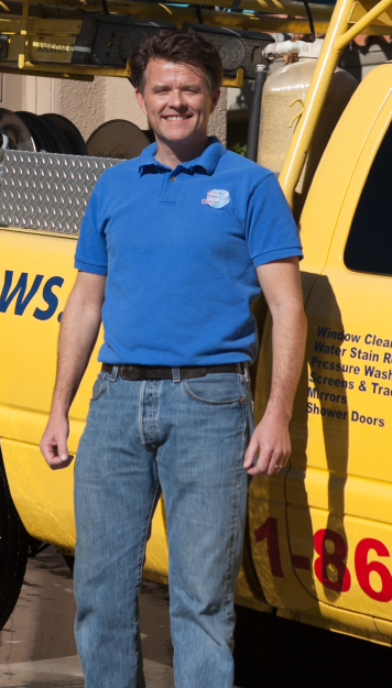 Tim Bloom stands in a bright blue shirt in front of a yellow truck outfitted with window cleaning supplies,