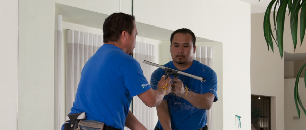 Inside, a window cleaner in a blue shirt uses a squeegee on a large mirror