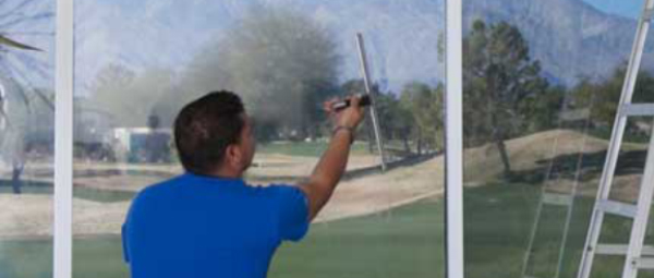 A window cleaner in a blue shirt uses a squeegee on a big reflective window. 